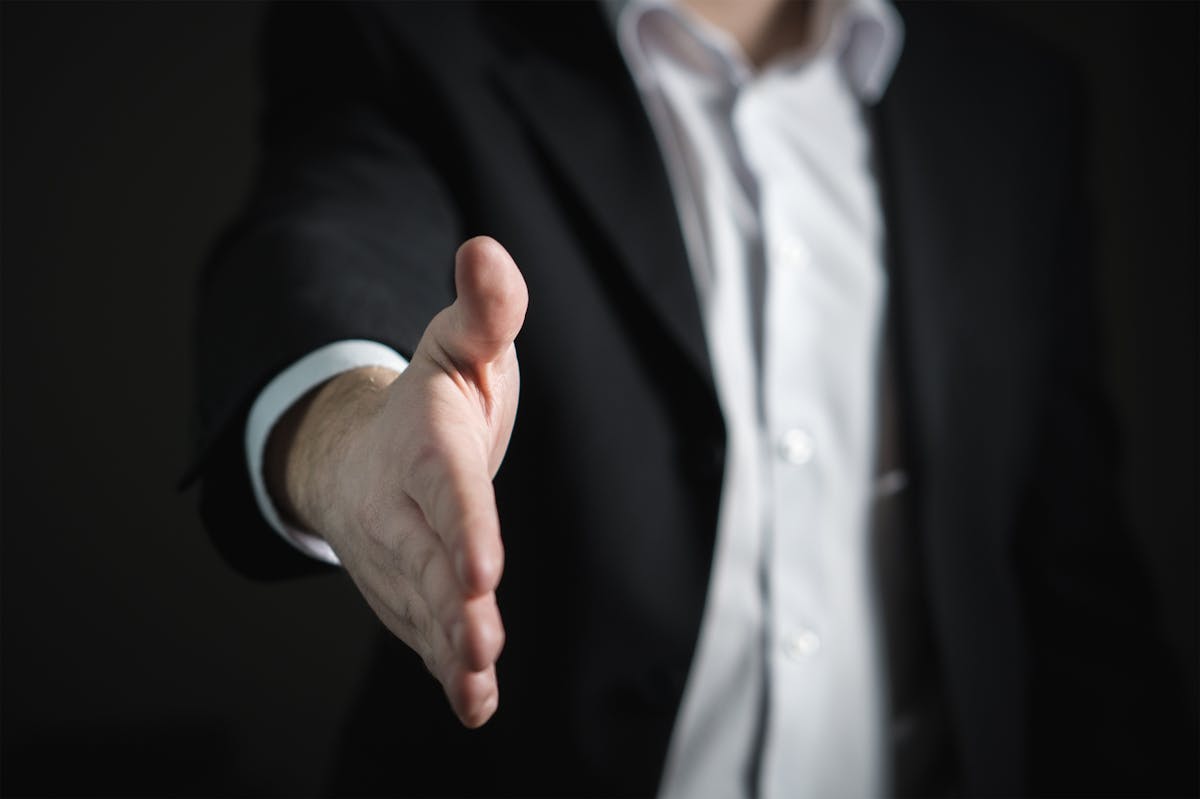 Reconversion Professionnelle à 40 ou 50 Ans : Témoignages et Guide Complet 2025 Close-up of a businessman extending hand for a handshake, symbolizing agreement and partnership.